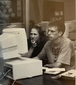 Two students read about an assignment on one of the computer lab in the library.