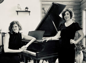 Black and white photo of two ladies by a piano. 