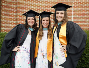 three graduates wear dresses decorated by their students
