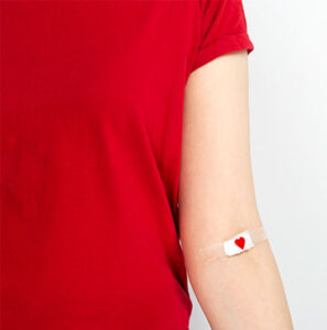 woman in red t-shirt with bandage on arm after giving blood