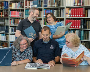 PHOTO OF five longtime employees in the library looking at yearbooks.