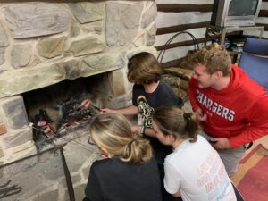 Students gather around the fireplace to roast s’mores and hotdogs. While many were disappointed about not being able to have a campfire outside, it was certainly fairer weather indoors.