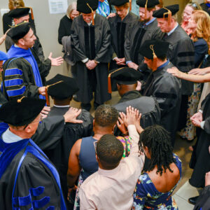 Dr. Kevin Gushiken, top left, prays with doctoral graduates in 2024.